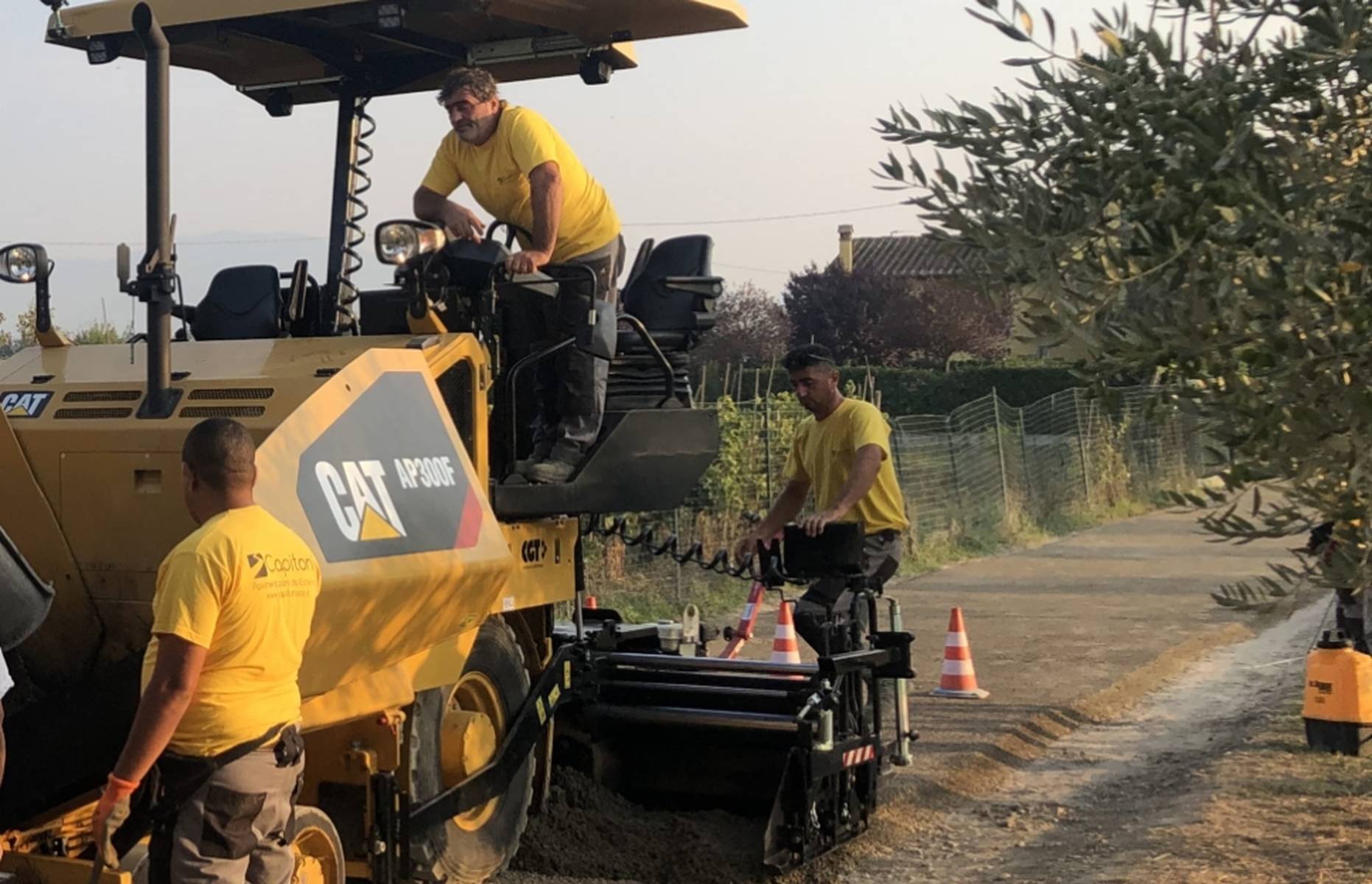 Operai su vibrofinitrice stendono uno strato permeabile e carrabile di calcestruzzo sul manto stradale sterrato di campagna.