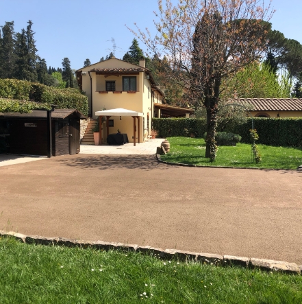 Pavimento permeabile attraversa il giardino di una villa con un bel prato in primo piano, ed alberi e cespuglio in fondo.