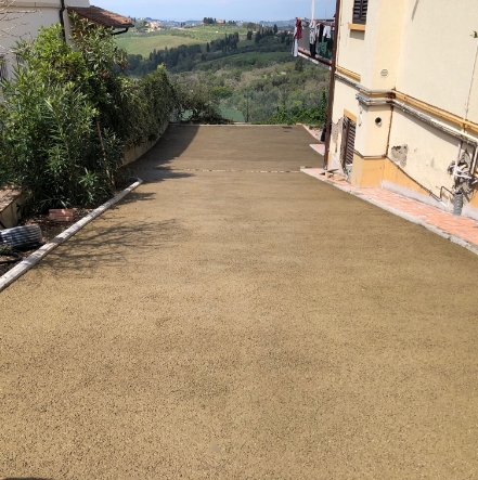 Pavimento permeabile in un resede privato, con vista su paesaggio collinare con edificio a destra ed aiuole a sinistra.