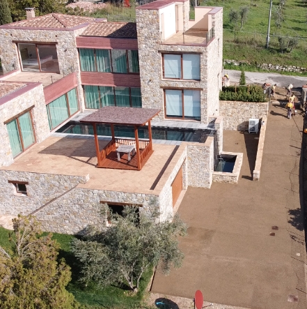 Rampa di accesso in drenante che conduce ad una villa con facciata in pietra e grandi vetrate, circondata da verde.