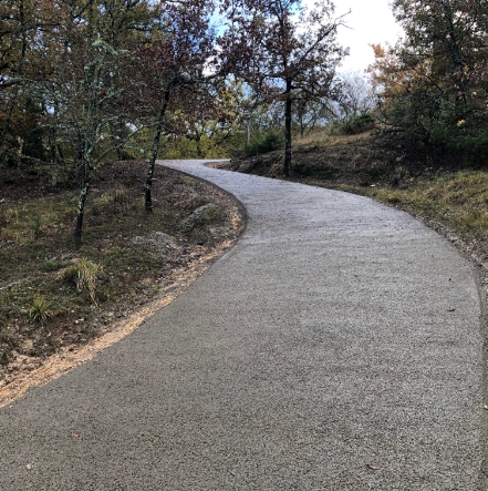 Strada pavimentata ricurva e in pendenza, ricoperta da calcestruzzo drenante, attraversa un paesaggio naturale autunnale con alberi e vegetazione.
