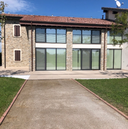 Vialetto pavimentato in calcestruzzo drenante che conduce a una casa moderna con facciata in pietra e grandi vetrate.
